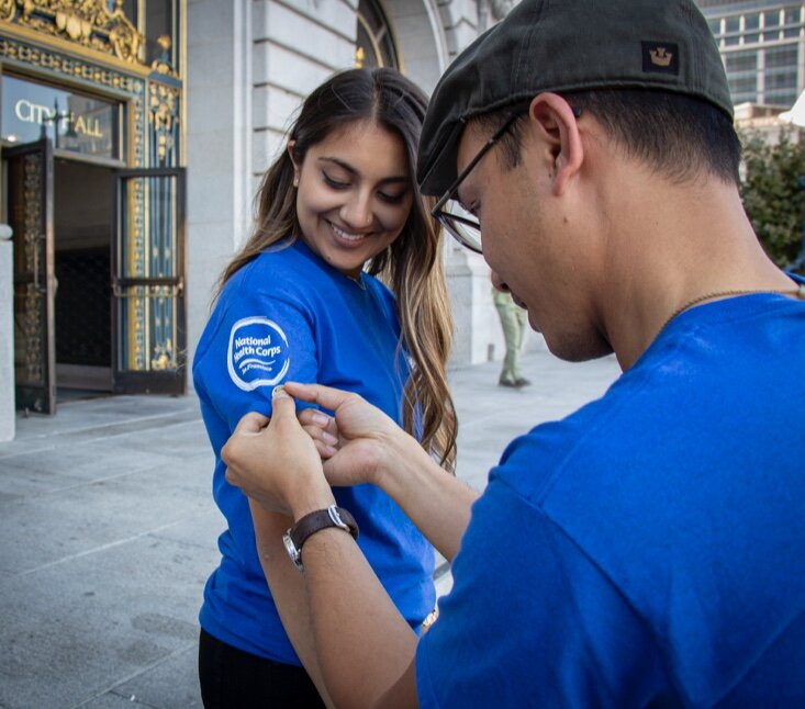 NHC SF AmeriCorps member Neha Chhabra getting her shirt pinned with the AmeriCorps Pin by Program Coordinator Nick Ragodos.