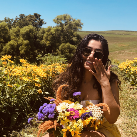 NHC PGH member Medha smiling in a field of flowers with sunglasses on and holding flowers