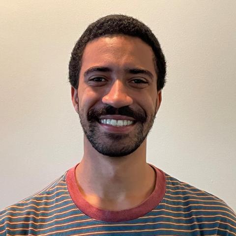 Amani Thurman smiling for the camera with a striped shirt and white wall background.