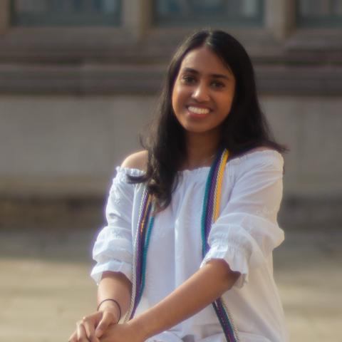 Anisha is sitting outside in front of a building.