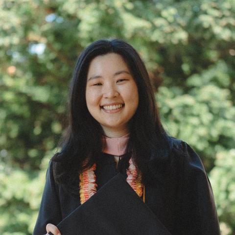 Jamie Lee is standing in the middle of the frame, facing the camera and smiling. Behind her is tree/brush foliage. 