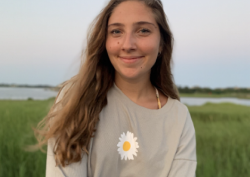 NHC PGH member Miranda soft-smiling in a field with a daisy on her sweatshirt