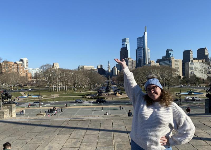 Emily standing on the "Rocky Steps" with the Philadelphia skyline in the background