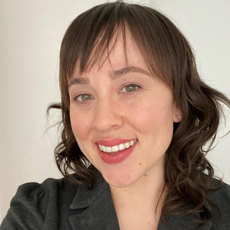 Hannah Griggs facing the camera while slightly turned to the right, smiling.Behind her is a white, blank wall.