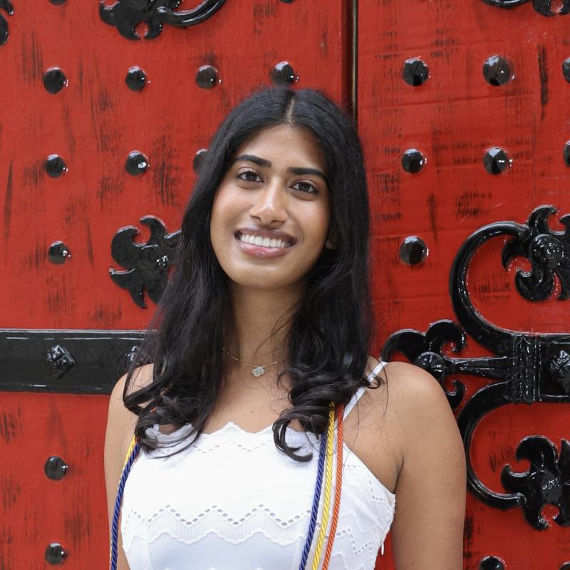 A headshot of Sanjana smiling in front of a red door